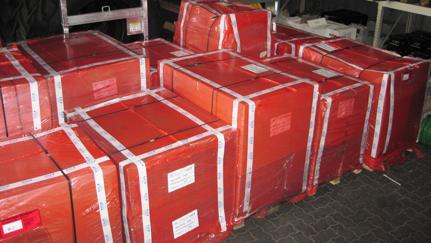 Airfreight consignment of automotive parts: Heavy cardboards on pallets, shrink-wrapped with resistant red RAC-Germany plastic film.